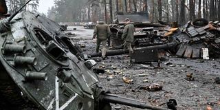 Ukrainian servicemen walk next to destroyed Russian tanks