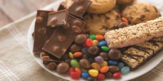 A close-up of chocolate, oatmeal cookies, drop candies and muesli bars on a plate.
