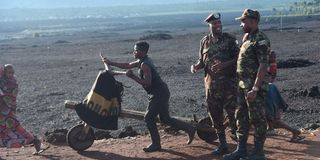 A Congolese man pushes a cart past KDF soldiers